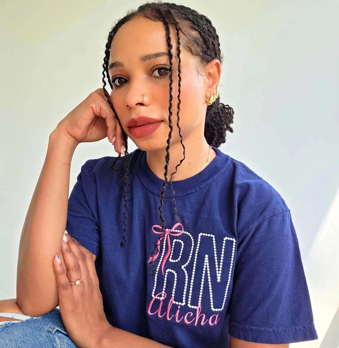 Woman wearing a blue shirt with 'RN Aticha' text, sitting against a light background.custom-nurse-shirt