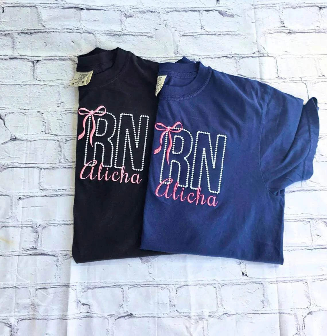 Two shirts with 'RN Alisha' text on a white brick background.custom-nurse-shirt