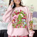 Person wearing a pink sweatshirt with a Christmas design, including a snowman, reindeer, and tree, in a festive setting.