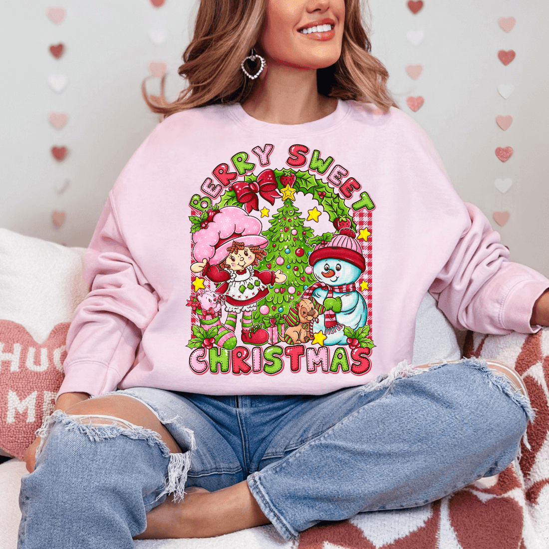 Person wearing a pink sweatshirt with a Christmas-themed design, sitting on a couch.