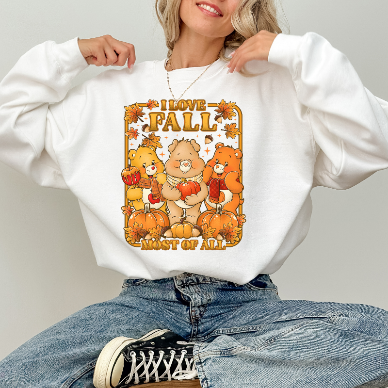Person wearing a white sweatshirt with 'I love fall most of all' design featuring cartoon bears and pumpkins. cozy-fall-bear-sweatshirt