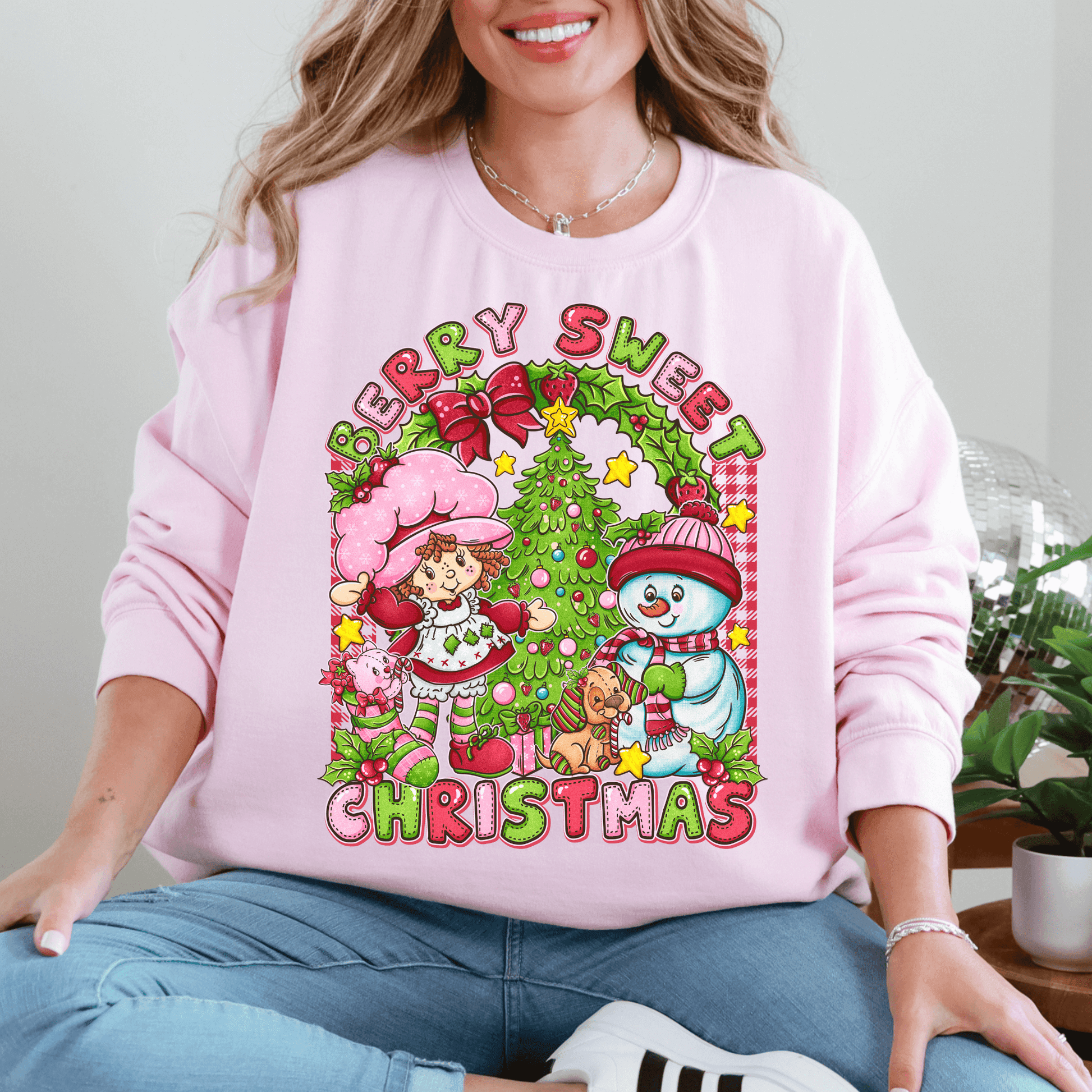 Person wearing a pink sweatshirt with Christmas-themed design featuring a snowman, tree, and cartoon characters.