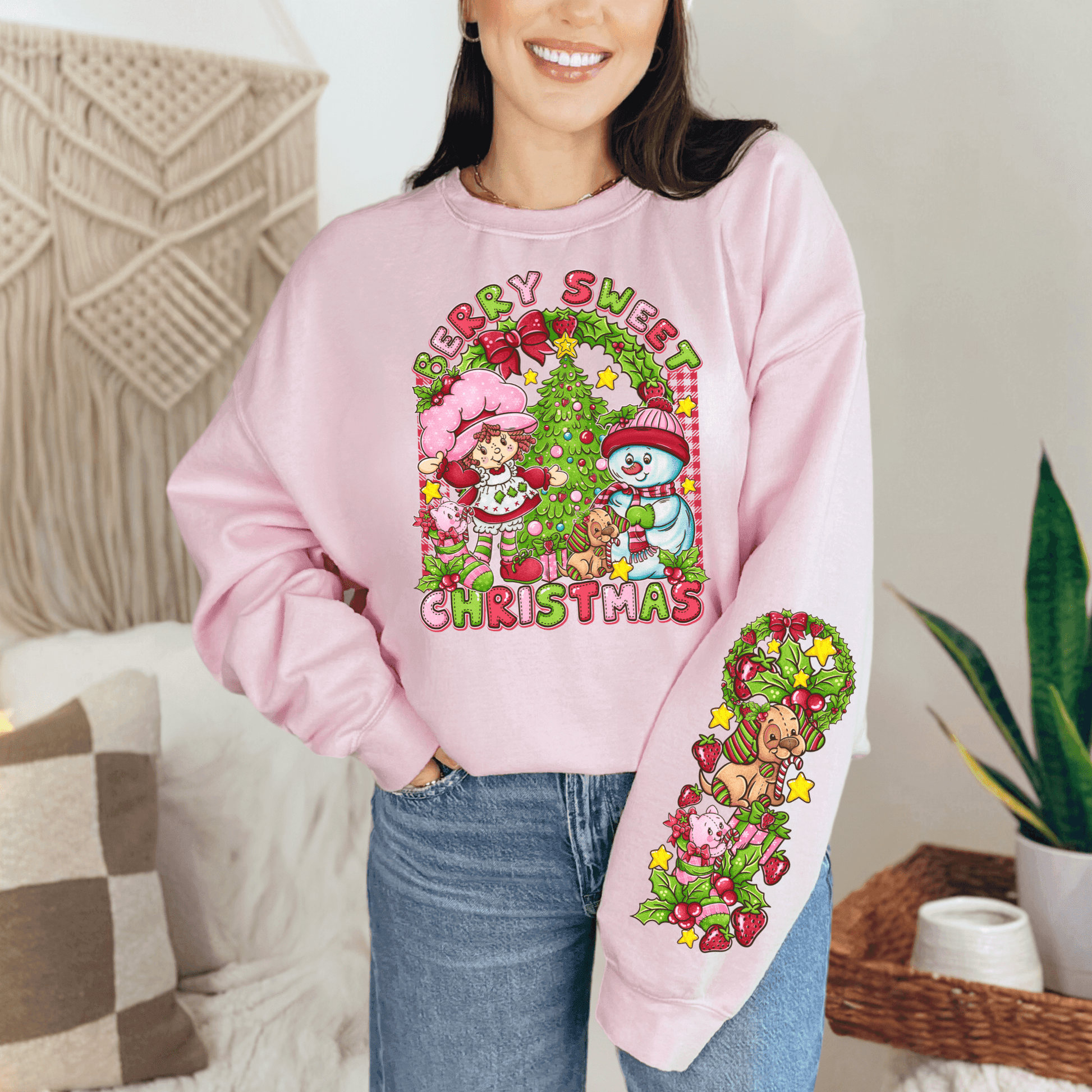 Person wearing a pink sweatshirt with Christmas-themed design in a cozy indoor setting.