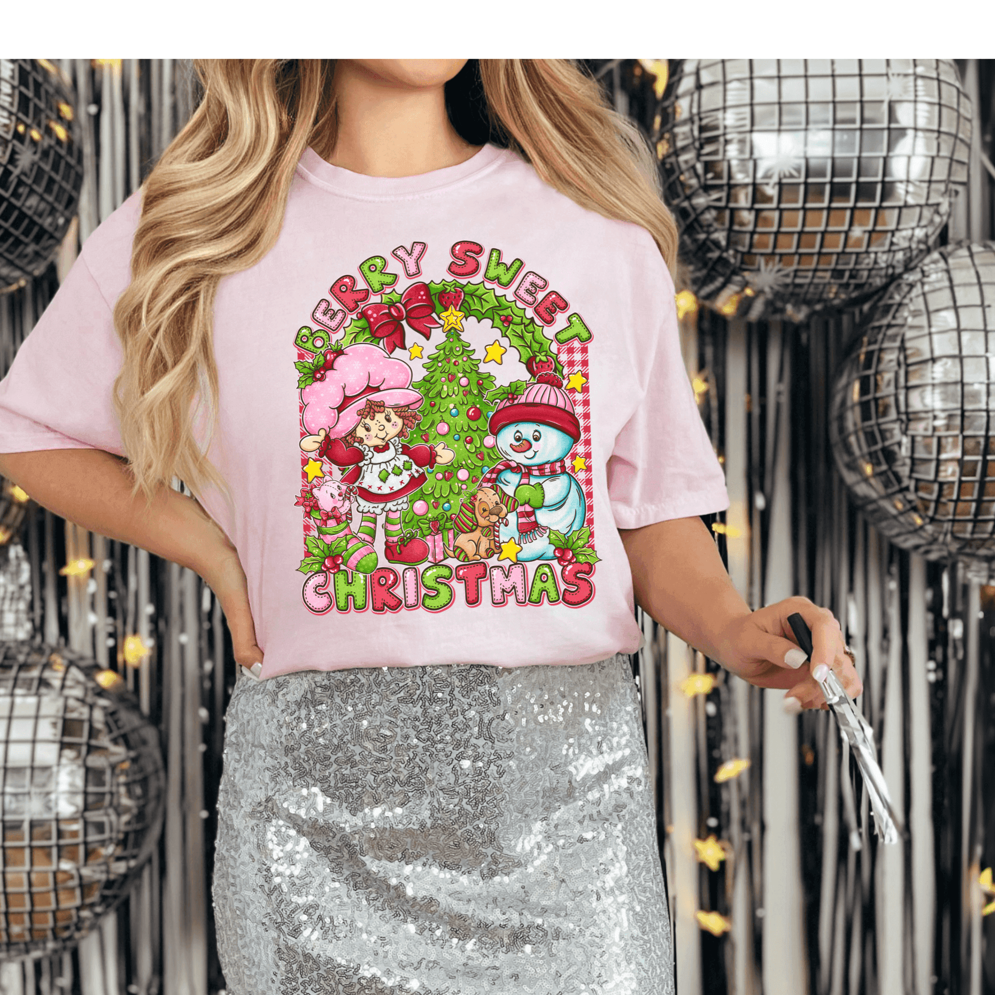 Person wearing a pink 'Merry Sweet Christmas' t-shirt with festive graphics against a disco ball background.