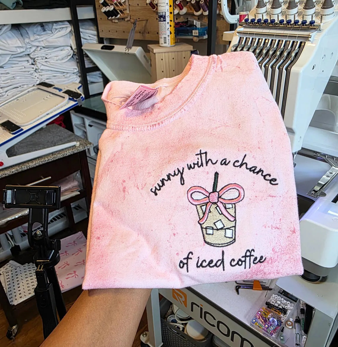 Pink tank top with text and graphic held in a workshop setting.but-first-coffee-shirt