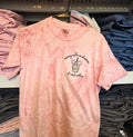 Pink tie-dye t-shirt with text and graphic on a hanger among folded shirts.but-first-coffee-shirt