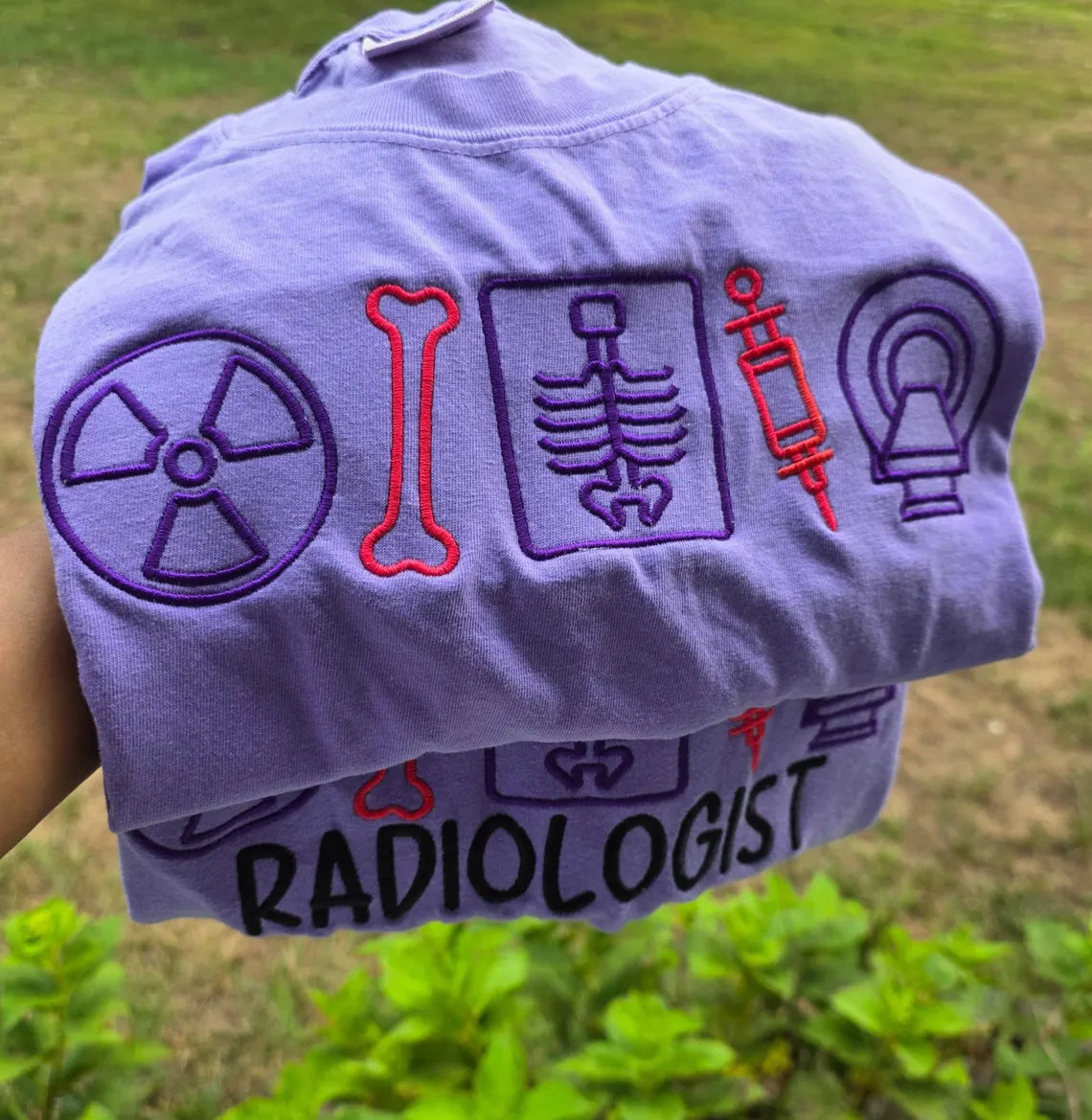 Folded shirt with radiology-themed designs and ' RADIOLOGIST' text on a grassy background.radiologist-t-shirt