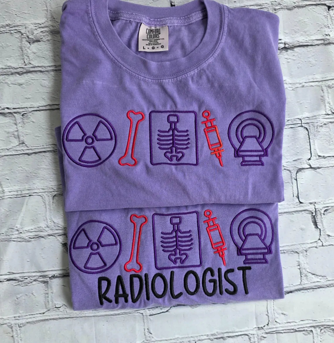 Folded purple t-shirt with radiology-themed graphics on a textured gray background.radiologist-t-shirt