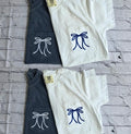 Two navy and two white t-shirts with bow designs on a textured gray surface