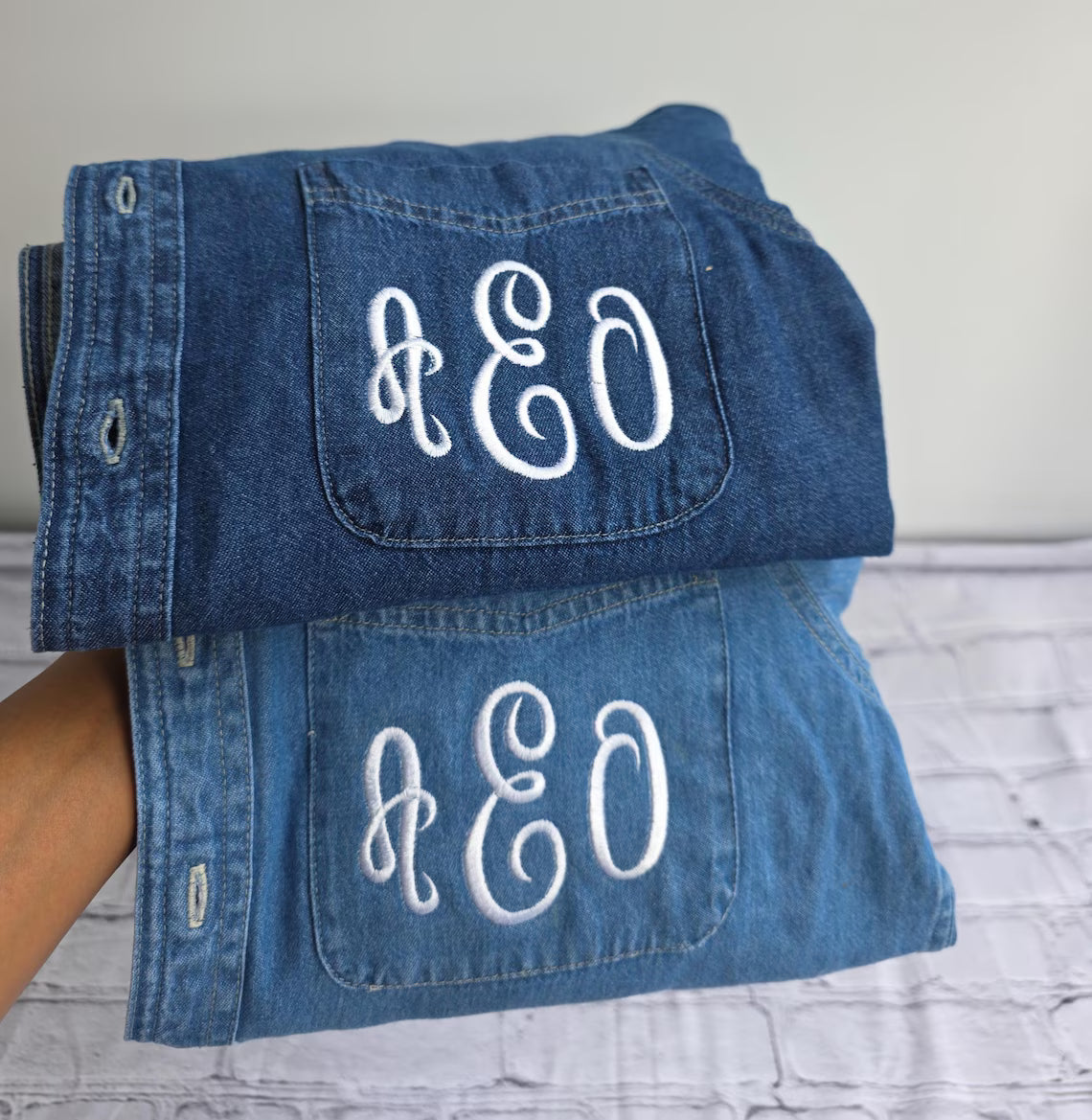 Folded denim jacket with 'AEO' monogram on a light gray surface.custom-bridesmaid-jackets