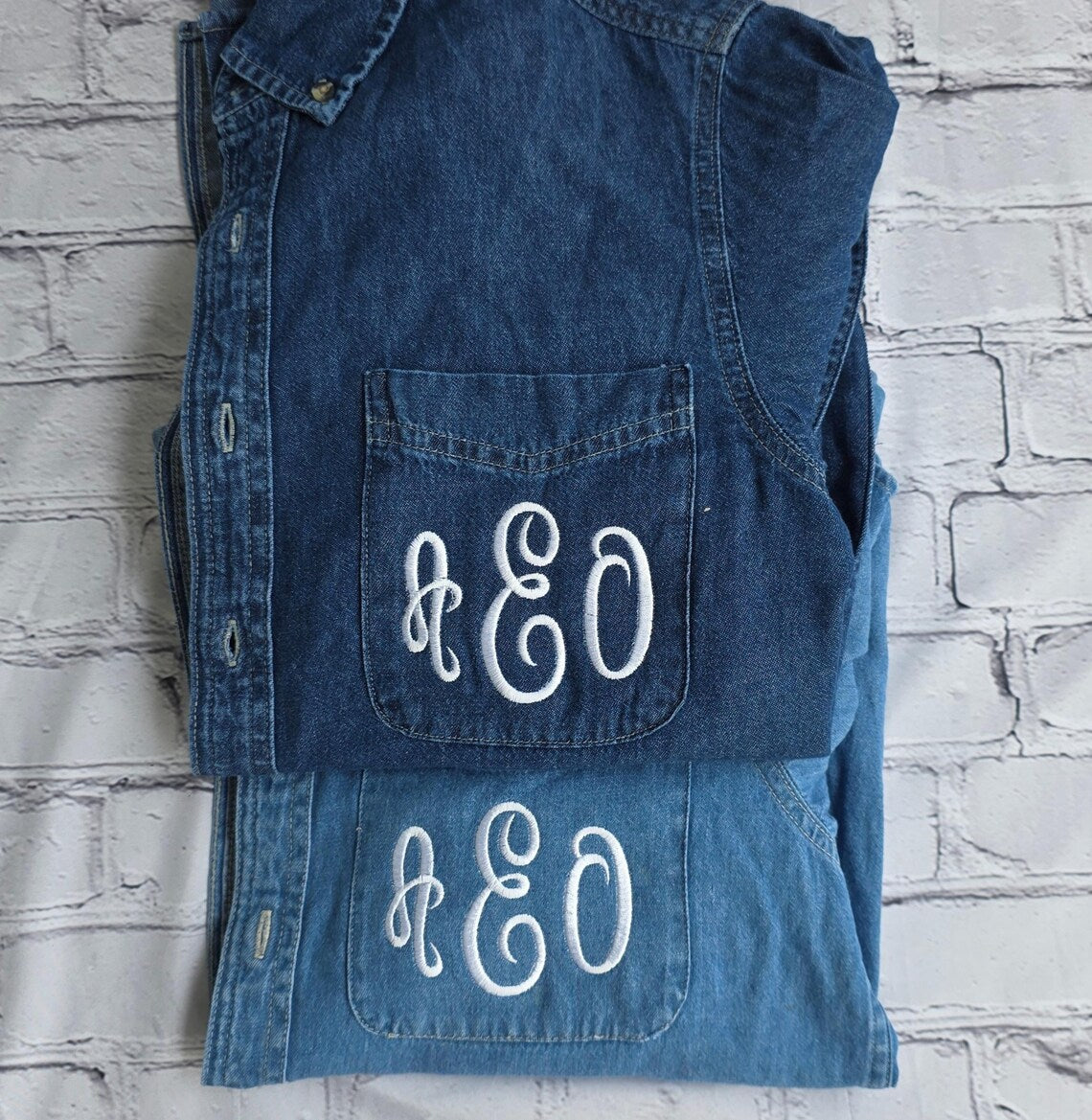Folded denim vest with 'A&EO' monogram on a textured white .custom-bridesmaid-jacketsbackground
