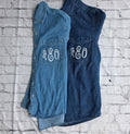 Two blue denim shirts with 'AEO' monogram on a white brick wall background.custom-bridesmaid-jackets
