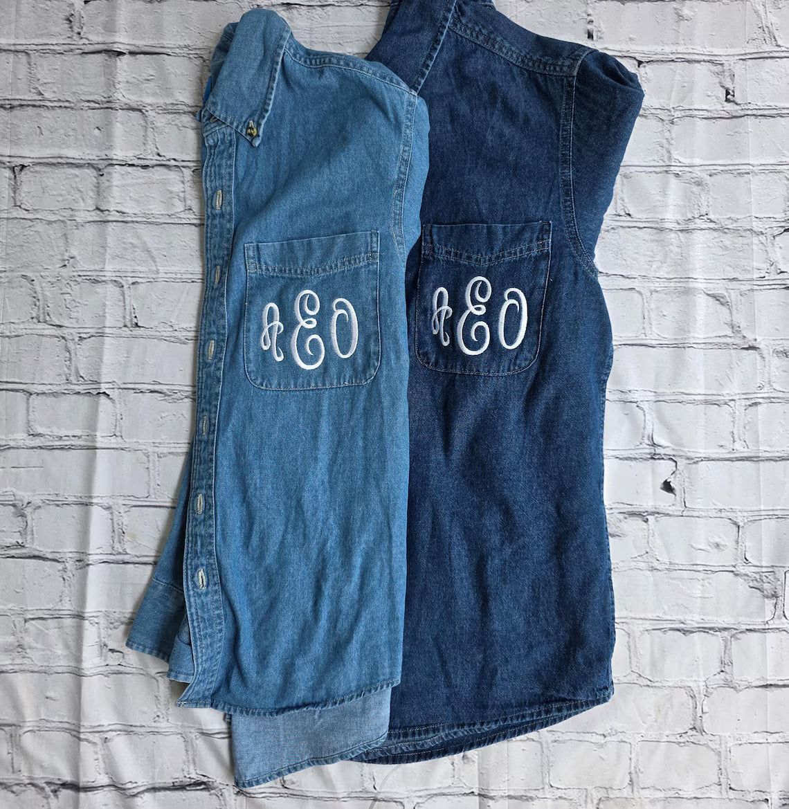 Two blue denim shirts with 'AEO' monogram on a white brick wall background.custom-bridesmaid-jackets