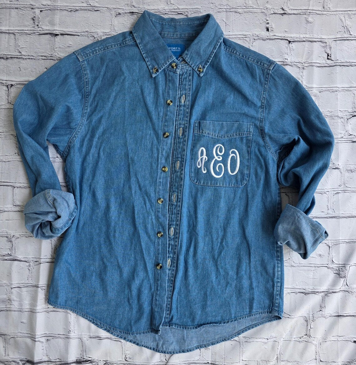 Blue denim shirt with a monogram on a textured white background.custom-bridesmaid-jackets