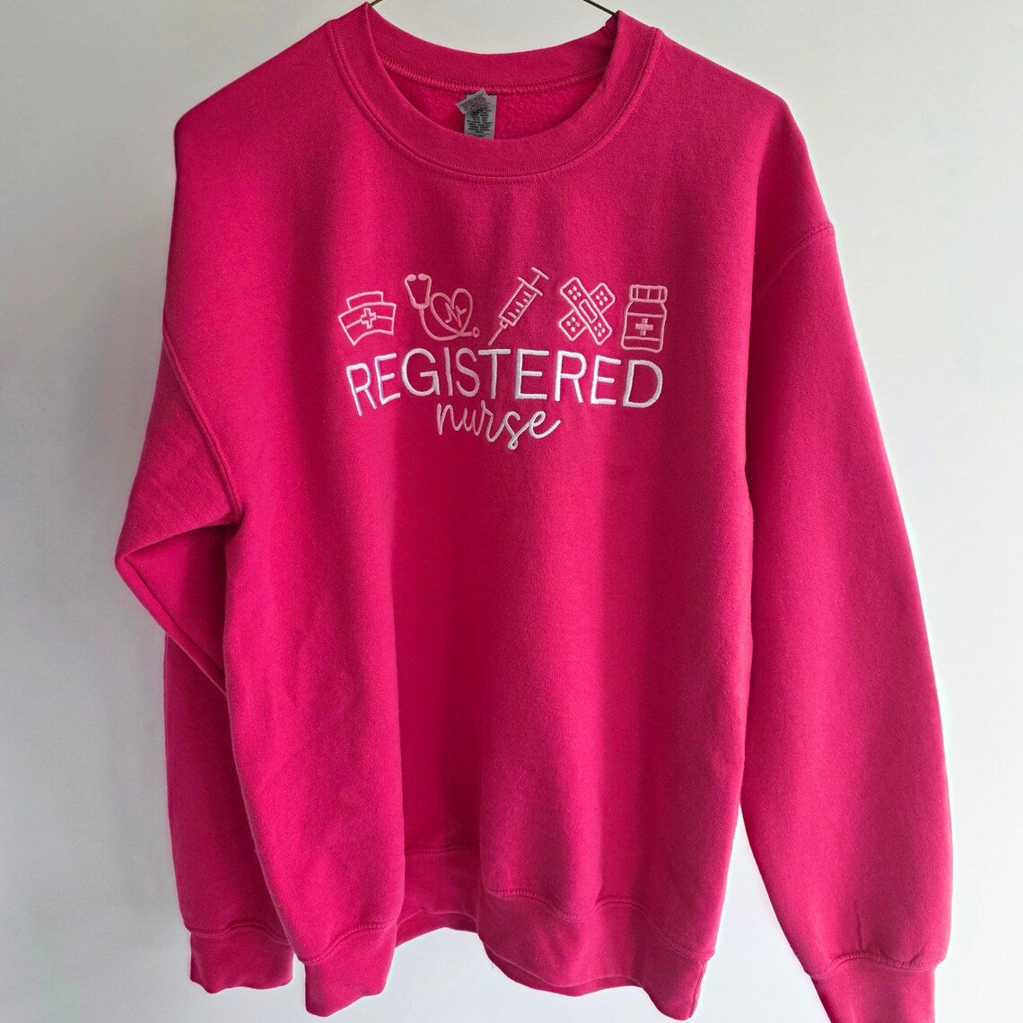 Pink sweatshirt with 'REGISTERED nurse' text and medical symbols on a white background.nurse-embroidered-sweatshirt