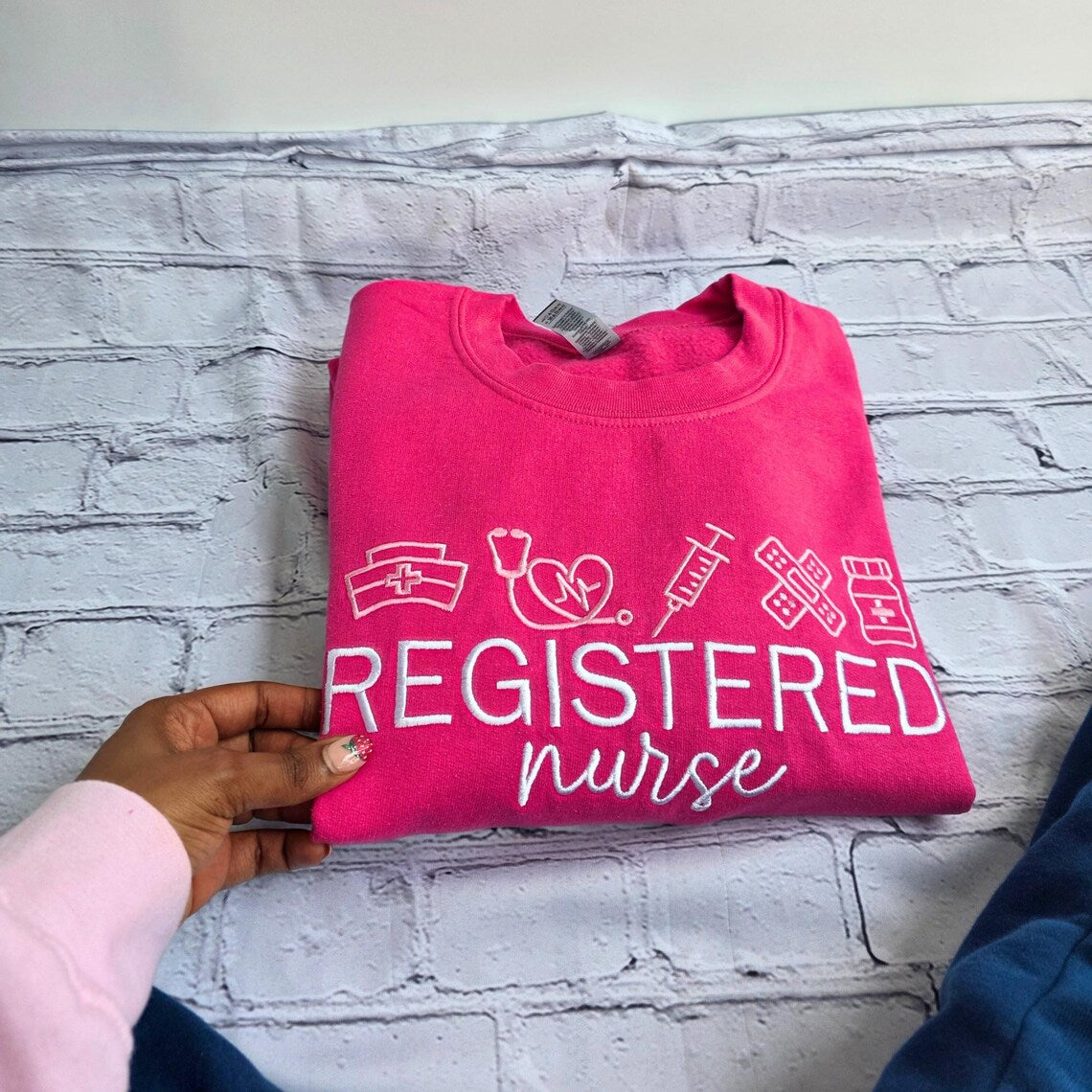 Pink sweatshirt with 'Registered Nurse' text and medical symbols on a textured surface.nurse-embroidered-sweatshirt