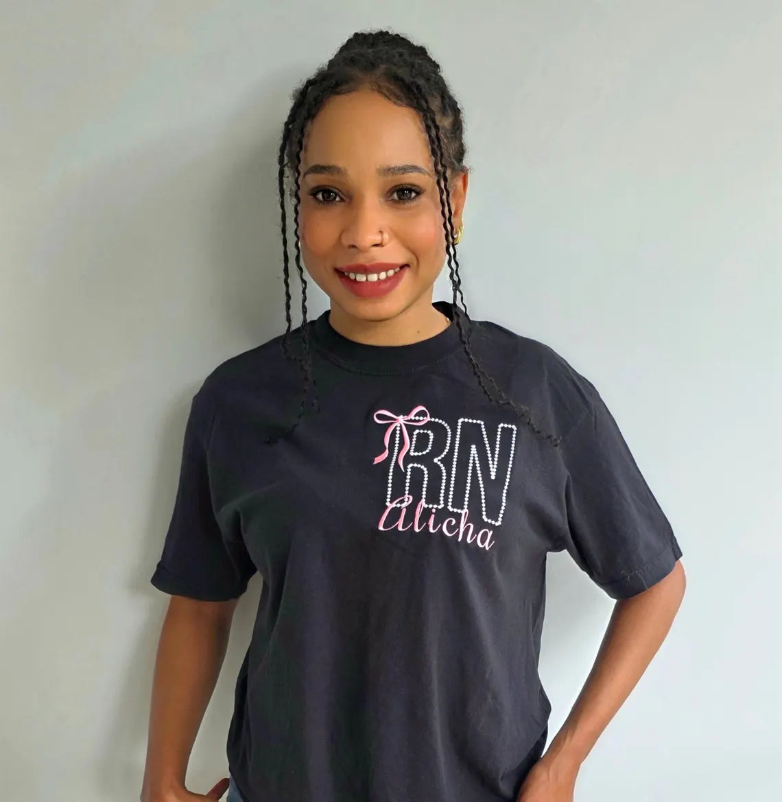 Person wearing a black t-shirt with 'RN' and 'Alitica' text on a plain background.custom-nurse-shirt