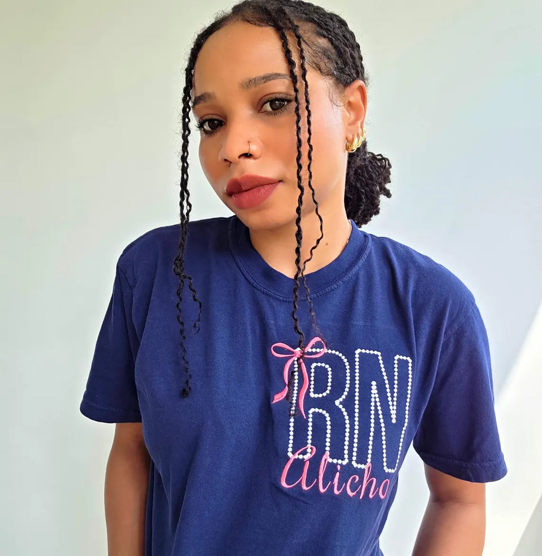 Two shirts with 'RN Alisha' text on a white brick background.custom-nurse-shirt