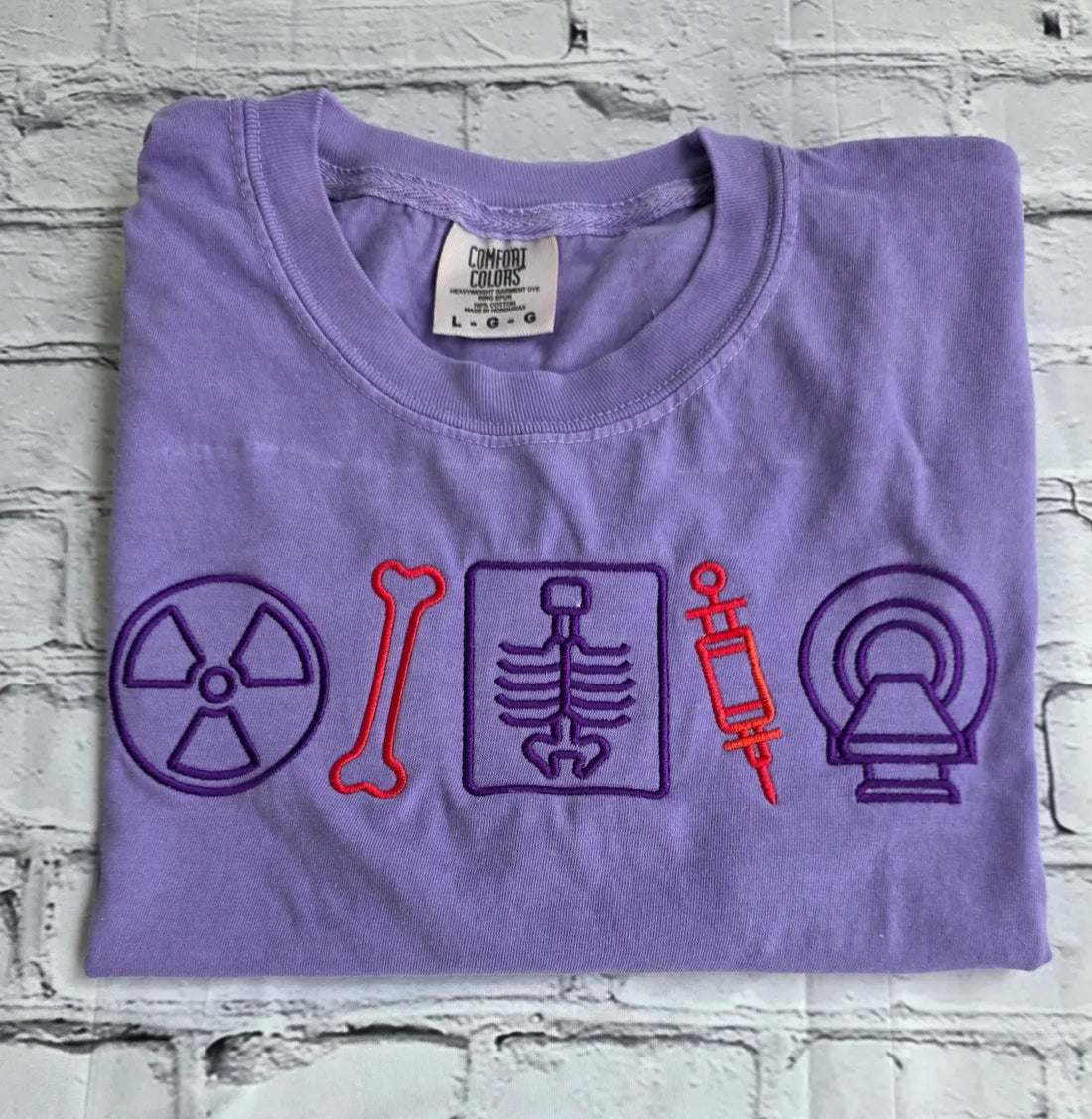 Folded purple t-shirt with medical-themed symbols on a textured surface.radiologist-t-shirt