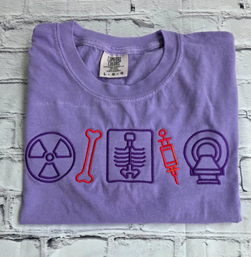 Folded purple t-shirt with medical-themed symbols on a textured surface.radiologist-t-shirt