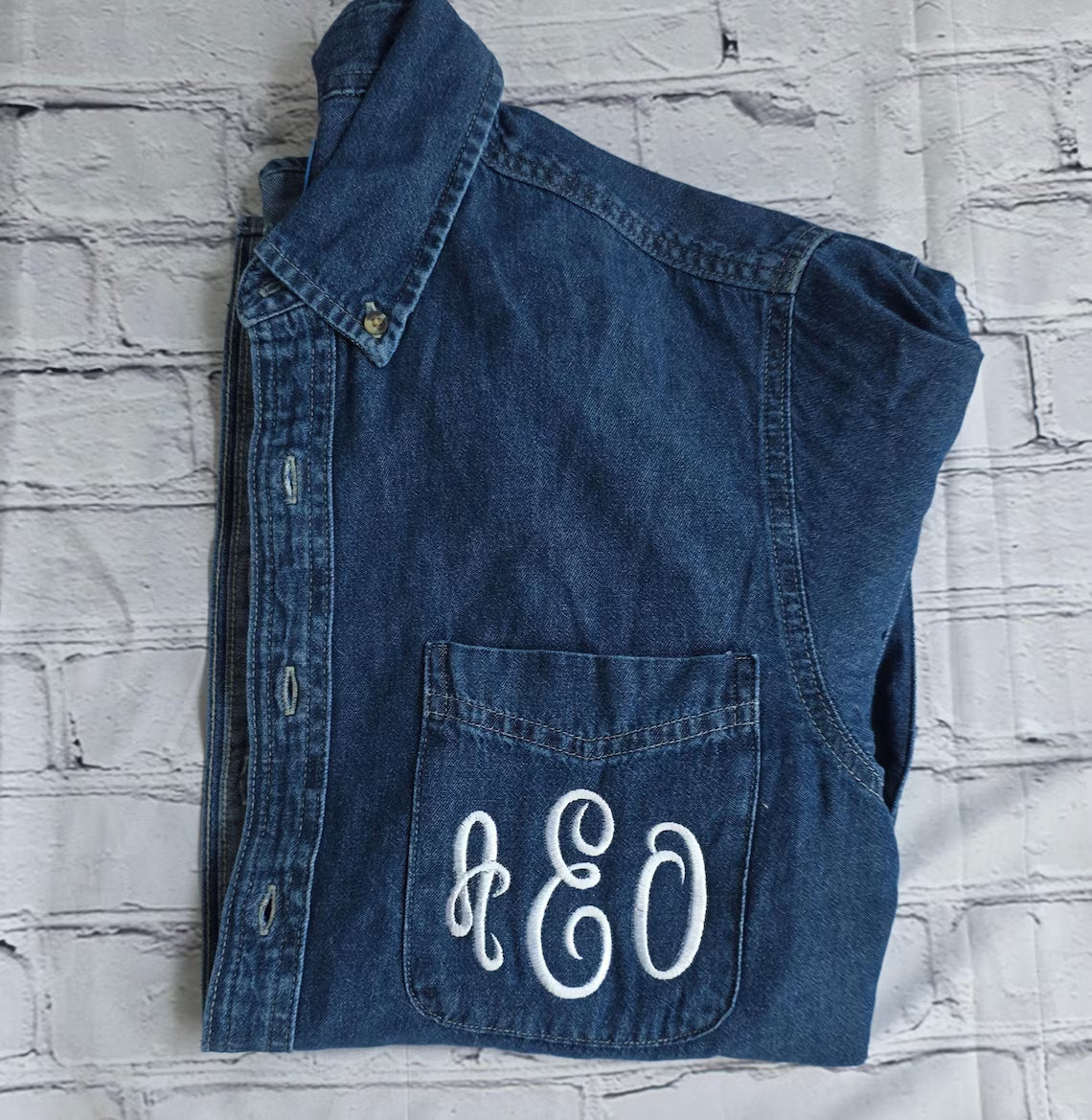 Blue denim vest with 'A&O' monogram on a textured white background.custom-bridesmaid-jackets