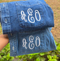 Blue denim jacket with 'A&O' monogram on a blurred green background.custom-bridesmaid-jackets