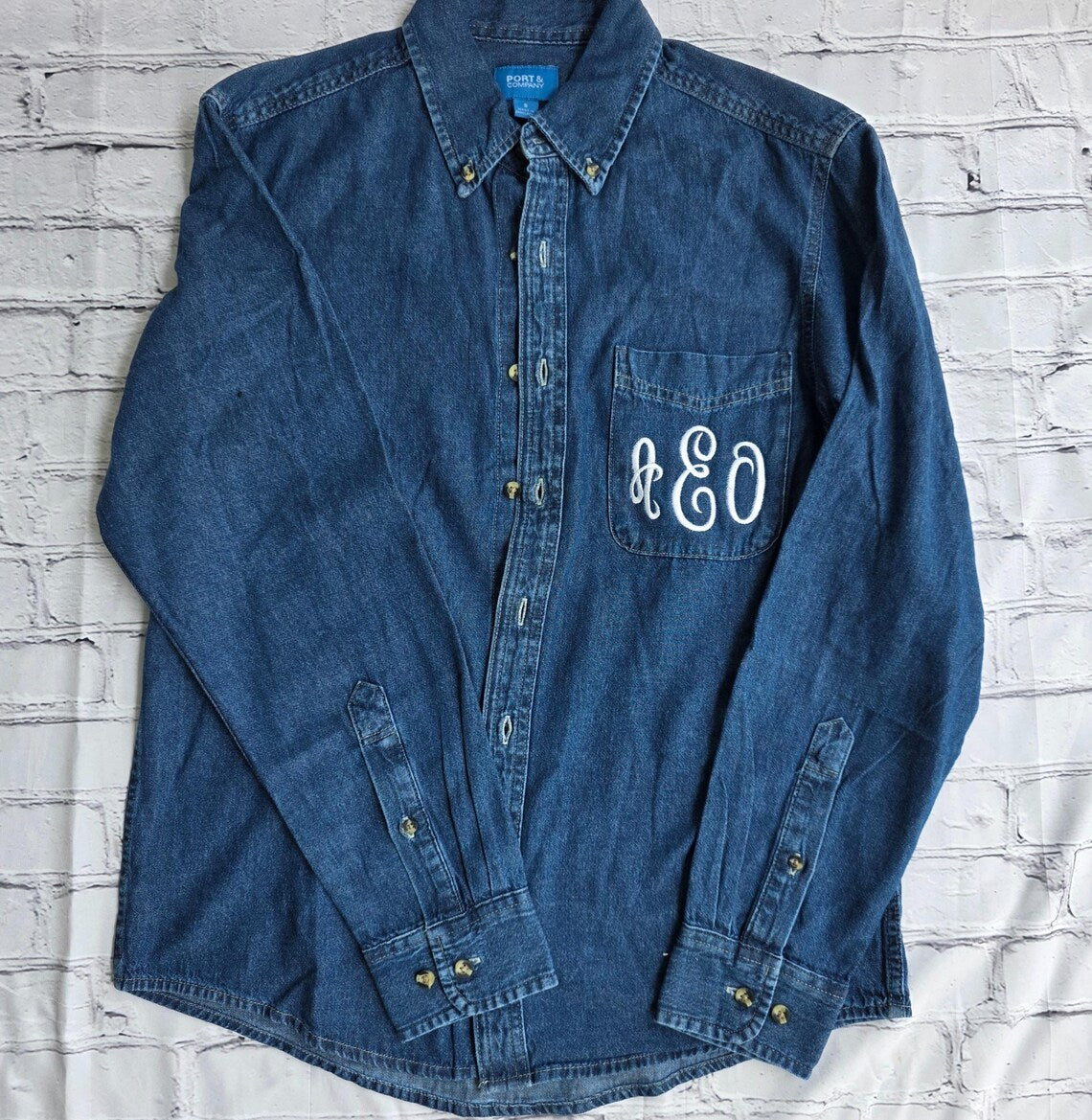 Blue denim shirt with monogram on a white brick wall background.custom-bridesmaid-jackets