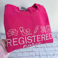 Pink sweatshirt with 'Registered Nurse' text and icons on a white background.nurse-embroidered-sweatshirt