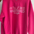 Pink sweatshirt with 'REGISTERED nurse' text and icons on a white .nurse-embroidered-sweatshirtbackground