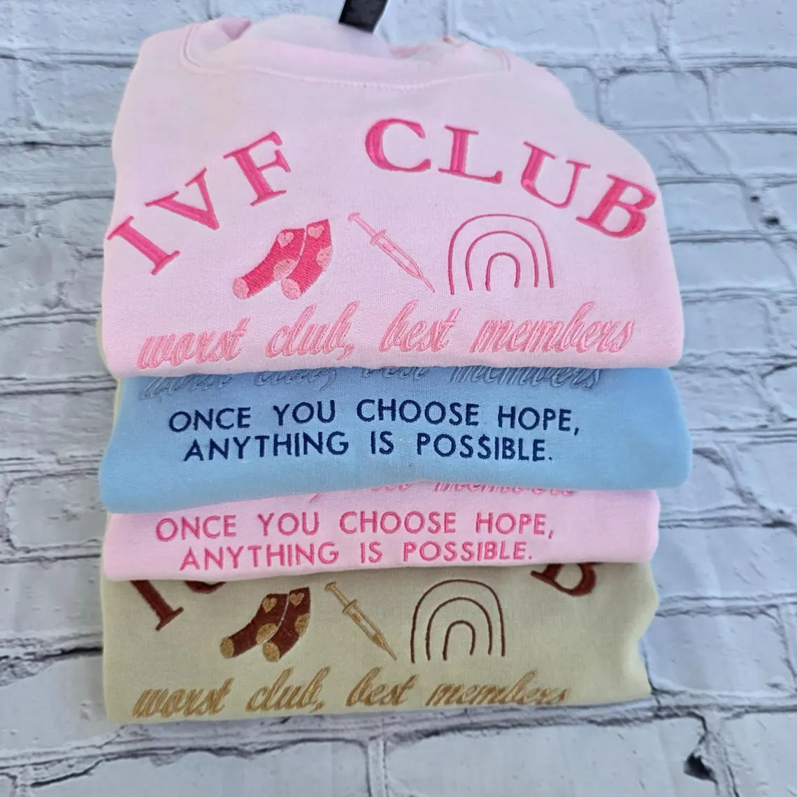Stack of baby bibs with motivational text and symbols on a textured surface. ivf-sweatshirt