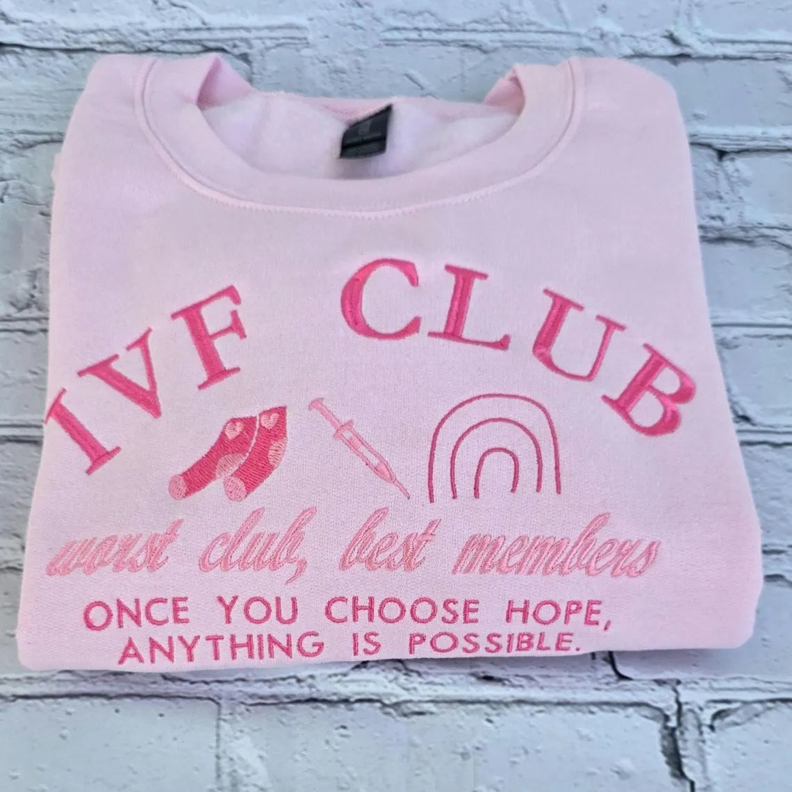 Pink sweatshirt with 'IVF Club' text and graphics on a textured surface