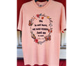 Stacked pink t-shirts with the text 'He is not here, HE HAS Risen' printed on them, placed on a red surface.