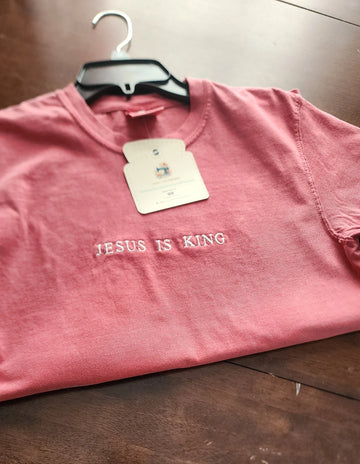 A pink short sleeve shirt with the phrase 'Jesus Is King' embroidered in a darker color across the front.jesus-is-king-shirt