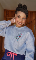 A person wearing a gray sweatshirt with an embroidered stethoscope and floral pattern on the chest.