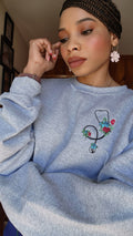 A person wearing a gray sweatshirt with an embroidered stethoscope and floral pattern on the chest.