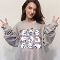 A woman wearing a light sweatshirt with a spooky nurse-themed design, including illustrations of ghosts and medical equipment, paired with black pants.