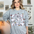 A woman wearing a sweatshirt with a spooky nurse-themed design, including illustrations of ghosts and medical equipment, paired with black pants.