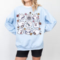 A woman wearing a light blue sweatshirt with a spooky nurse-themed design, including illustrations of ghosts and medical equipment, paired with black pants.