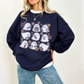 A woman wearing a sweatshirt with a spooky nurse-themed design, including illustrations of ghosts and medical equipment, paired with black pants.