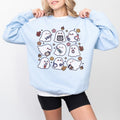A woman wearing a  sweatshirt with a spooky nurse-themed design, including illustrations of ghosts and medical equipment, paired with black pants.