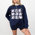 A woman wearing a light blue sweatshirt with a spooky nurse-themed design, including illustrations of ghosts and medical equipment, paired with black pants.