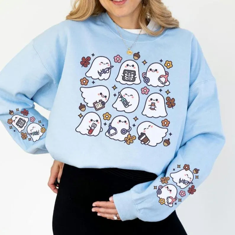 A woman wearing a light blue sweatshirt with a spooky nurse-themed design, including illustrations of ghosts and medical equipment, paired with black pants.