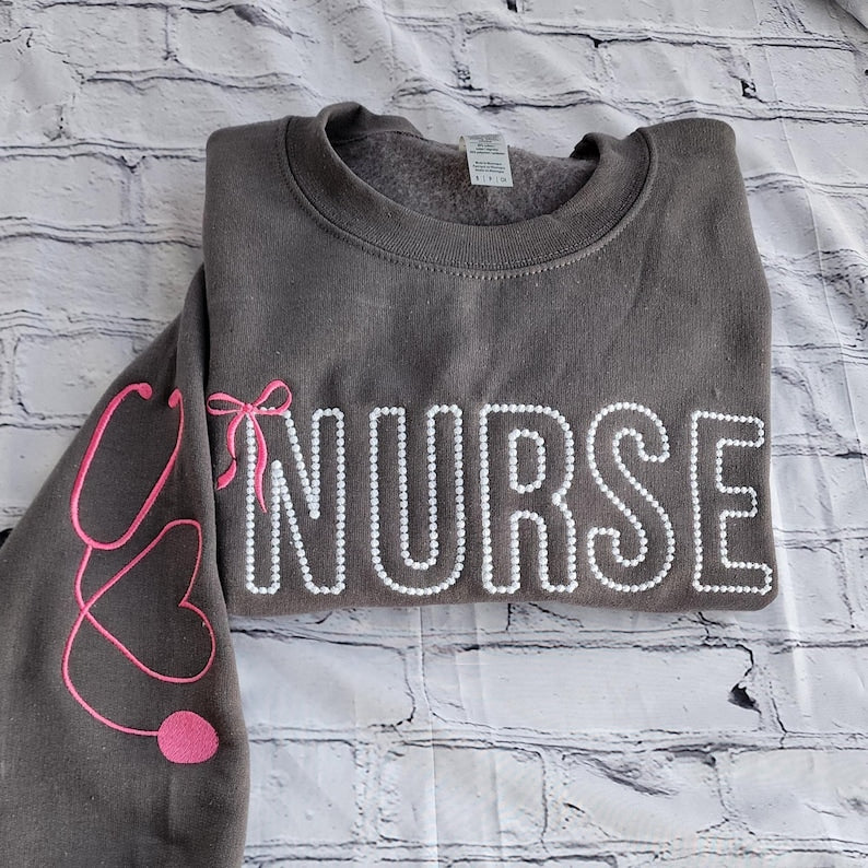 A collection of custom embroidered grey nurse shirts with various titles and names embroidered on the left side of the chest.