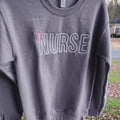 A collection of custom embroidered grey nurse shirts with various titles and names embroidered on the left side of the chest.