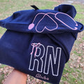A collection of custom embroidered grey nurse shirts with various titles and names embroidered on the left side of the chest.