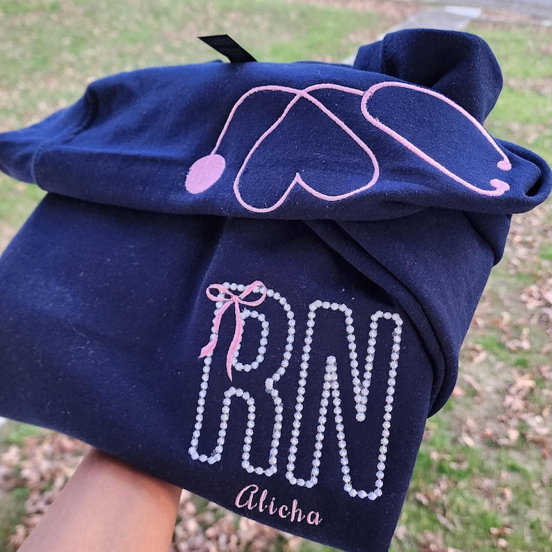 A collection of custom embroidered grey nurse shirts with various titles and names embroidered on the left side of the chest.