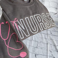 A collection of custom embroidered grey nurse shirts with various titles and names embroidered on the left side of the chest.