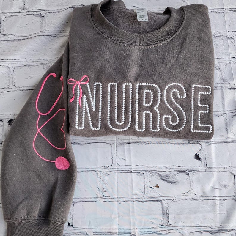 A collection of custom embroidered grey nurse shirts with various titles and names embroidered on the left side of the chest.