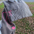 A collection of custom embroidered grey nurse shirts with various titles and names embroidered on the left side of the chest.