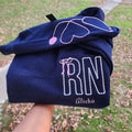 A collection of custom embroidered grey nurse shirts with various titles and names embroidered on the left side of the chest.